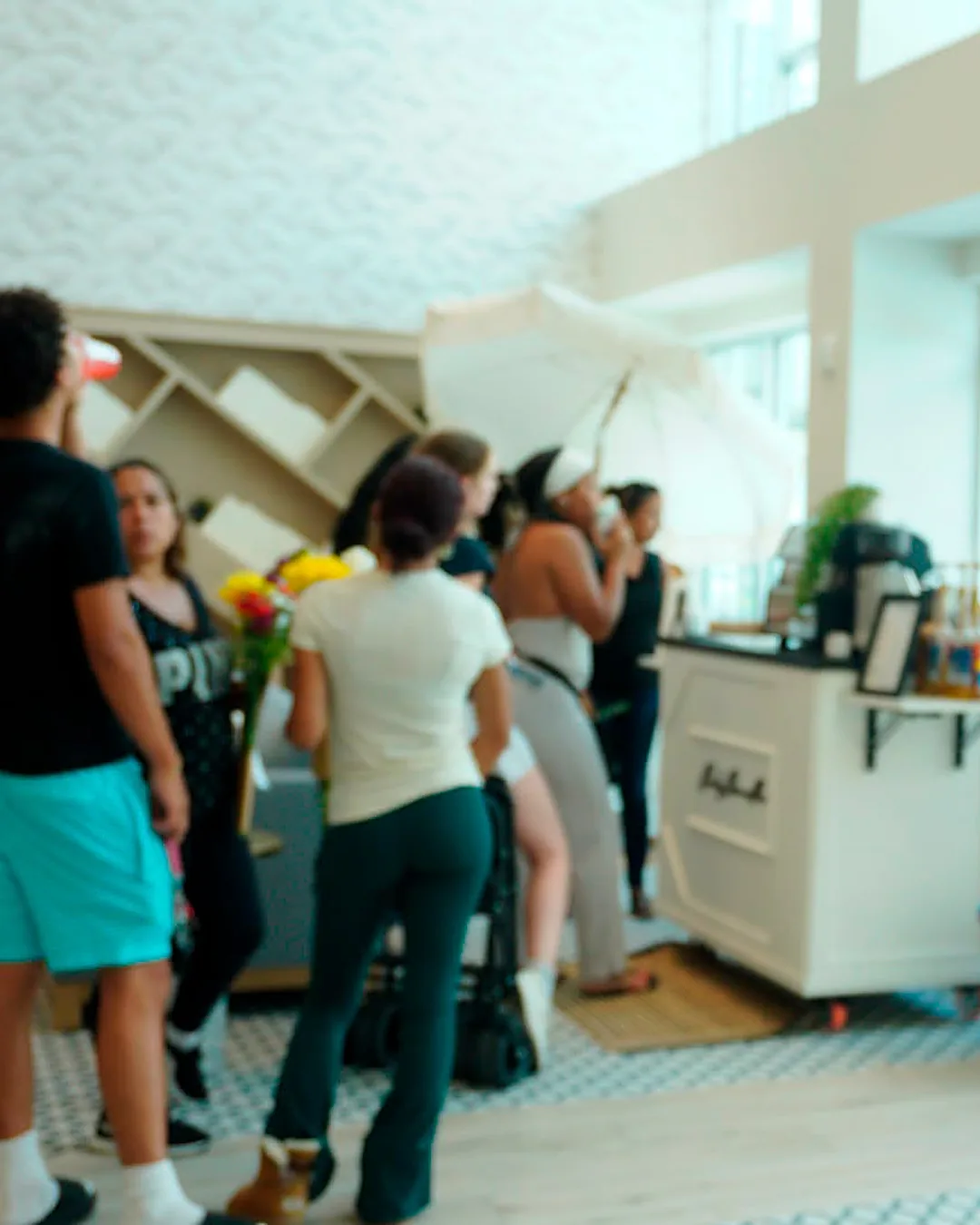 Guests waiting and drinking at the Daily Dose cart under its fringed umbrella in a bright residential lounge