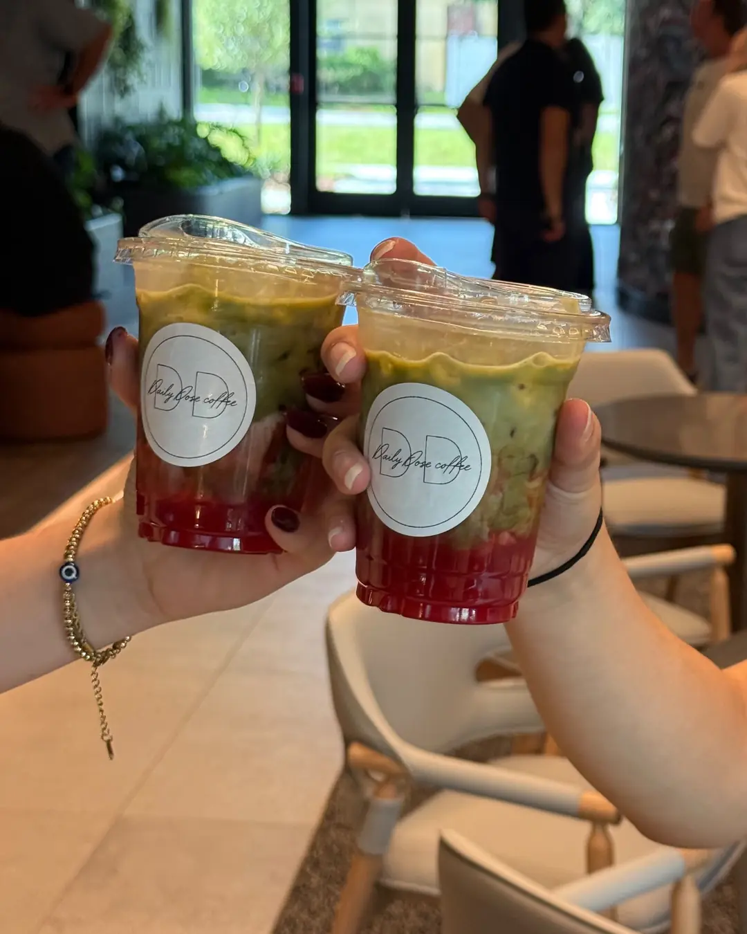 Two guests toast with layered strawberry matcha lattes in clear cups, each sealed with a round Daily Dose sticker